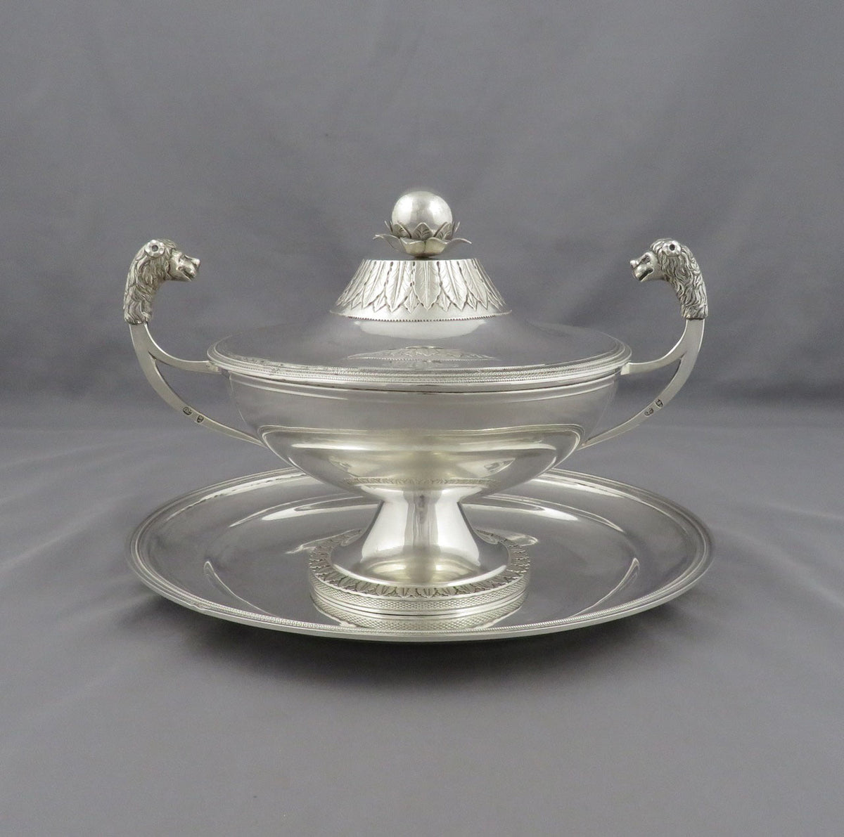 An antique Italian sterling silver tureen with, Kingdom of Sardinia c. 1820,. featuring lion's head handles and a matching serving tray, set against a neutral gray background.