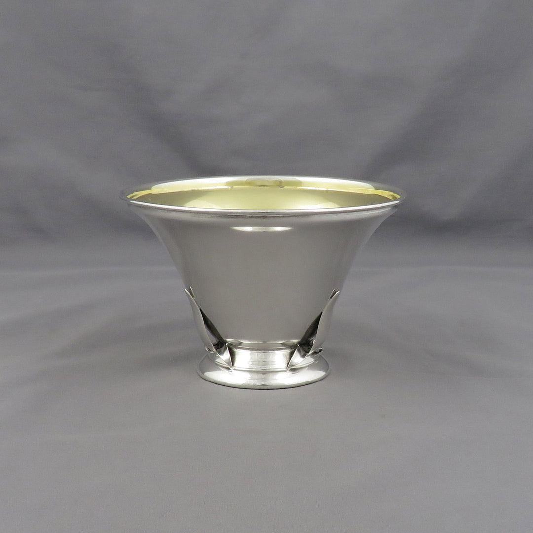 A polished silver pedestal bowl with a flared rim and a small base, photographed against a neutral gray fabric backdrop.