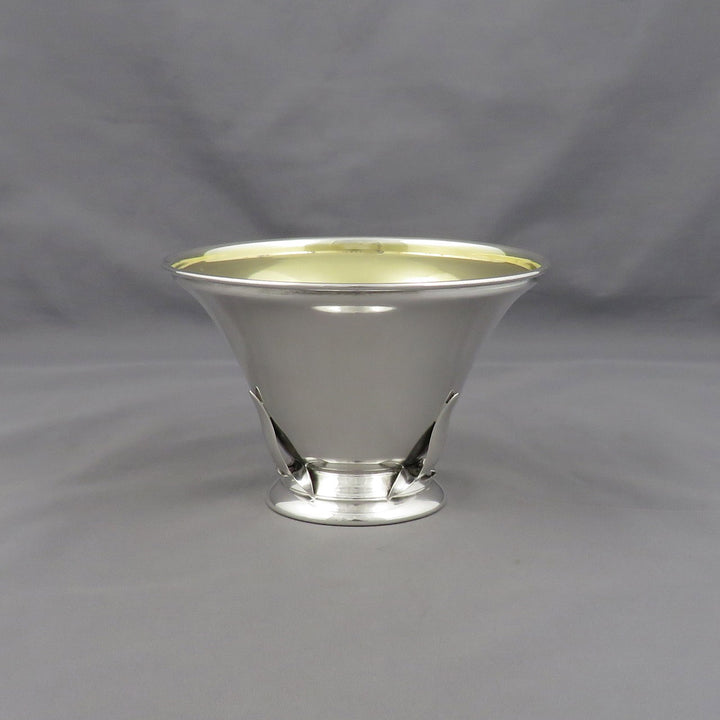 A polished silver pedestal bowl with a flared rim and a small base, photographed against a neutral gray fabric backdrop.